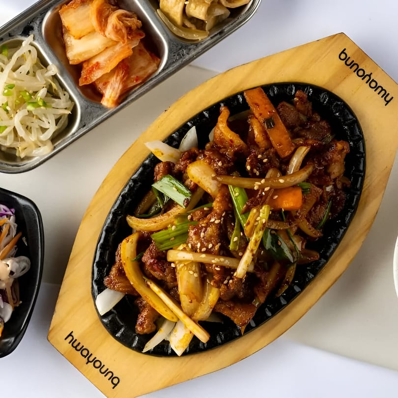Spicy Korean pork bulgogi sizzling on a black plate with kimchi and bean sprouts.